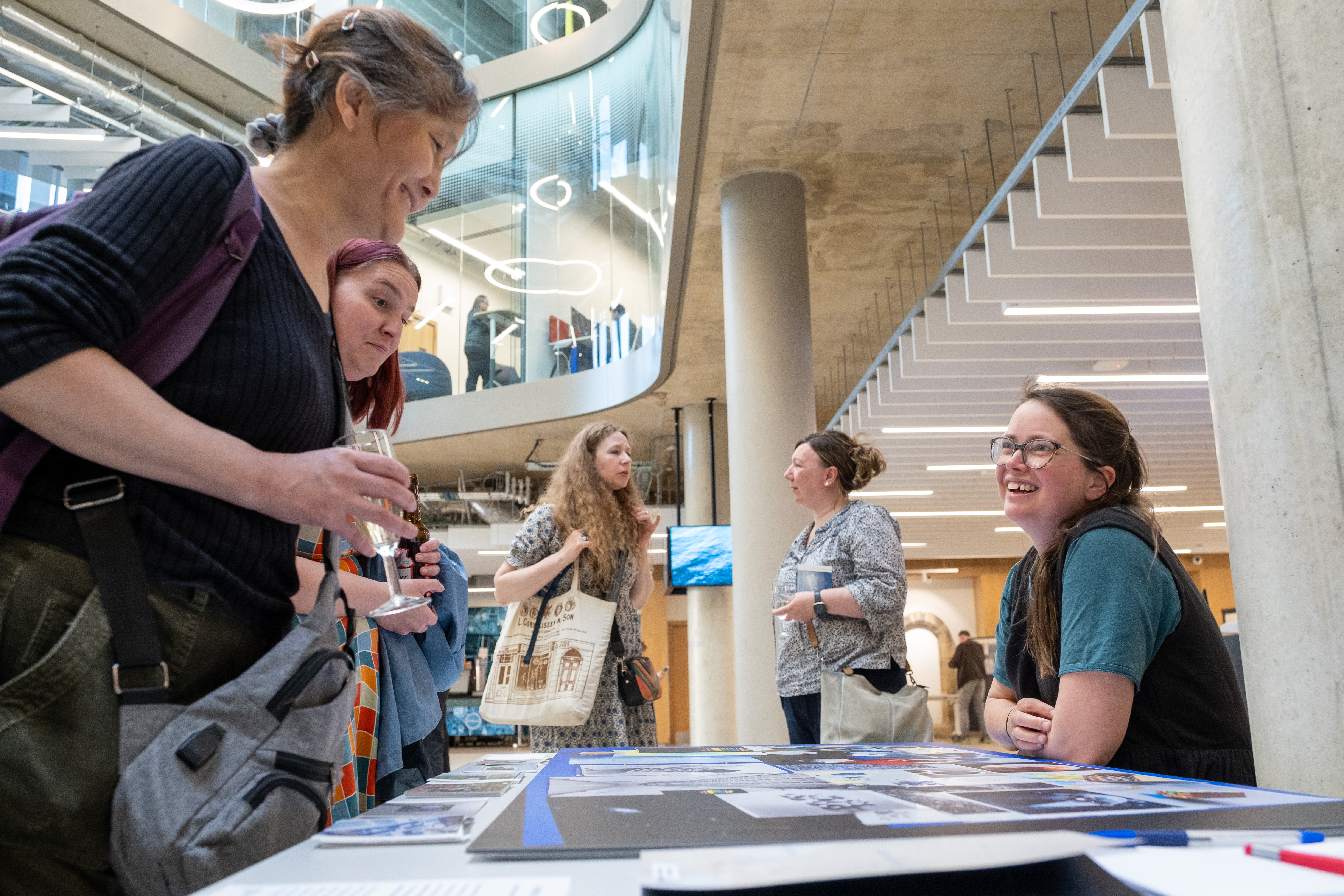 two women look at large visual displays on table, woman behind table smiles at them